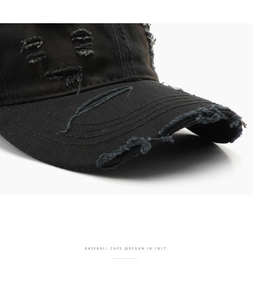 Close-up of distressed denim texture and frayed holes on a vintage black baseball cap