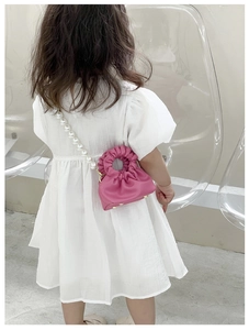 Detail view of mini fuchsia crossbody bag with large pearl strap worn by a child