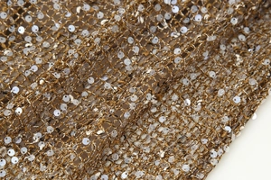 Gros plan détaillé des sequins dorés cousus sur tissu en maille pour robe de soirée