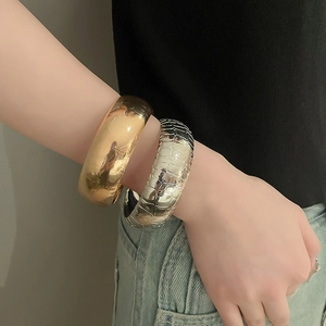 Detail of wide metallic bracelets with textured crocodile pattern in gold and silver finish