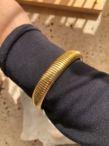 Gros plan d'un bracelet Tubogas doré porté sur une manche noire sous la lumière du soleil