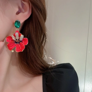 Close-up of vibrant red floral earrings with sparkling crystals on a model's ear
