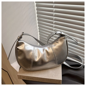 Detailed view of silver metallic leather crescent bag resting on a gray book
