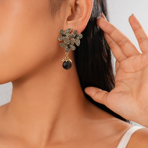Detailed view of floral gold earrings with pavé crystals and faceted black bead charms