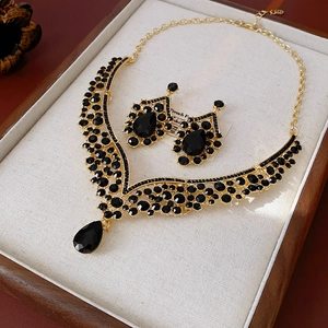 Macro shot of V-shaped gold necklace and teardrop earrings set with black crystals