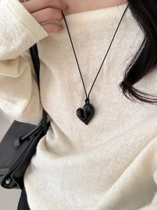 Dettaglio della collana con cuore nero e cordino regolabile su un maglione lavorato
