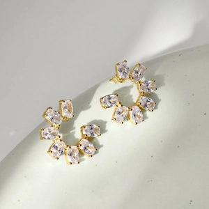 Detailed view of gold C-shaped earrings with sparkling oval zircon stones on grey surface