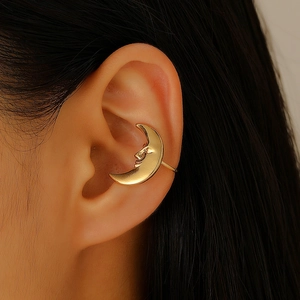 Detailed close-up of a golden crescent moon ear cuff with a smiling face relief design