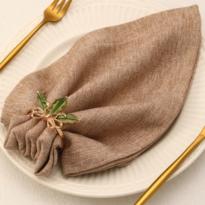 Détail d'un rond de serviette nœud doré avec feuilles en émail vert sur serviette en lin