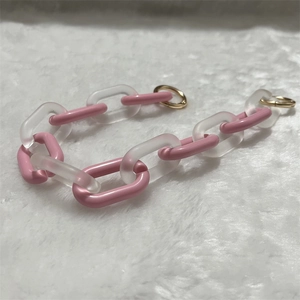 Detail of pink acrylic chain accessory with golden round metal clasps on plush background