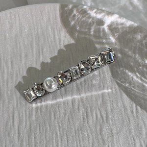 Detail of silver hair clip featuring crystal shapes and a white pearl on white surface