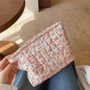 Dettaglio di una trousse trapuntata in cotone a fiori tenuta in mano da una modella