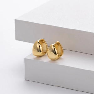 Close-up of golden teardrop earrings on a white geometric stand with elegant lighting