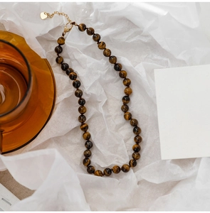 Close-up of tiger eye beaded necklace with gold lobster clasp and heart charm on white paper