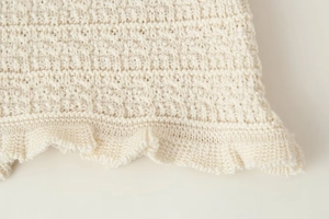Gros plan sur la texture de la maille blanc crème et le design de l'ourlet à volants