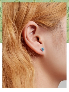 Close-up of blue and purple floral silver stud earrings worn on a female ear