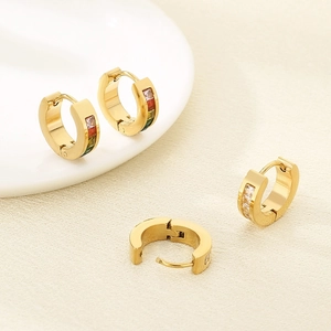 Boucles d'oreilles créoles en acier doré avec zircons colorés sous un éclairage doux