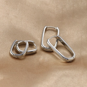 Close-up of two pairs of silver U-shaped geometric earrings on a golden silk fabric backdrop