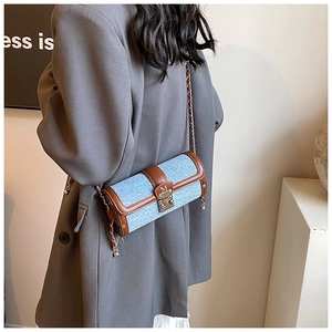 Detailed side view of a cylinder crossbody bag with denim and brown leather trim