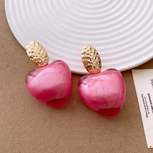 Close-up of pink resin heart earrings with golden hammered metal clasp on desk