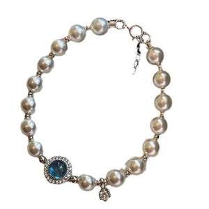 Silver pearl bracelet with blue round gemstone and floral pendant on white background