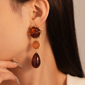 Detail of amber acrylic teardrop earrings with gold trim worn by a model in retro style