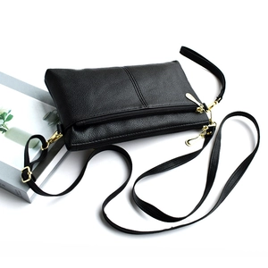 Close-up of black pebble leather crossbody bag with golden zippers and adjustable strap
