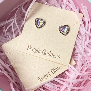 Close-up of heart-shaped iridescent stud earrings on jewelry card with pink gift box