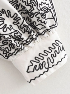 Vue macro détaillée d'une broderie noire sur manchette blanche avec motifs géométriques