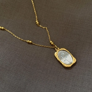 Golden titanium steel necklace with a rectangular rose pendant on a textured background