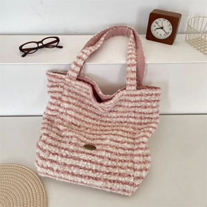 Detail of pink striped plush tote bag featuring soft fleece fabric and metal logo plaque