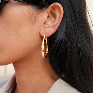 Close-up of golden twisted teardrop earrings worn by a model to show elegant metal texture