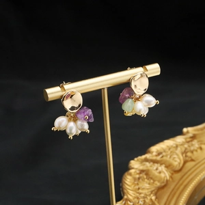 Elegant natural pearl and purple gemstone earrings on a gold stand with black background