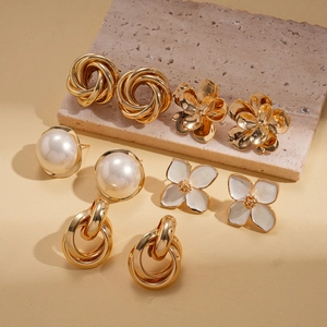 Macro shot of 5-pair gold earring set with faux pearls and white floral enamel details