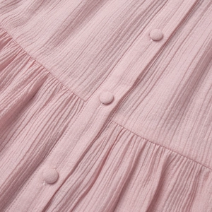 Detailed macro view of light pink pleated fabric and matching cloth buttons on women's set