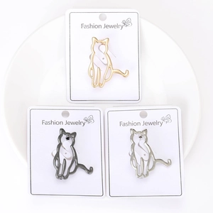Three minimalist cat-shaped brooches in gold, silver and black on white cards