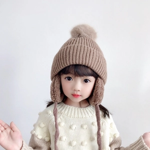 Close-up of brown knitted winter hat with faux fur pom-poms and ear protection ties