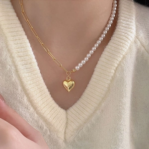 Detail of asymmetrical necklace with gold heart pendant, paperclip chain and pearls