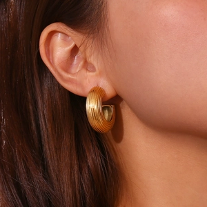 Gros plan de boucles d'oreilles créoles torsadées dorées en C sur un mannequin