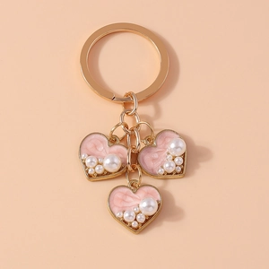 Close-up of golden keychain with three pink enamel heart pendants and faux pearls