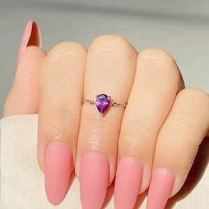 Gros plan d'une bague avec pierre violette en poire et anneau en chaîne dorée fine