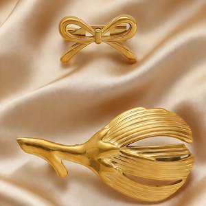 Macro shot of gold bow brooch and textured leaf pin on champagne satin fabric