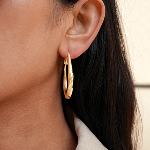 Detail of a golden twisted teardrop hoop earring worn by a model for a stylish look