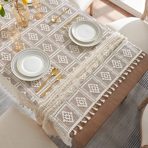 Elegant beige hollow lace table runner with tassels on a wooden dining table setting