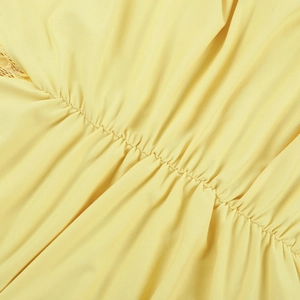 Macro detail of yellow fabric with delicate pleats and intricate lace patchwork finish