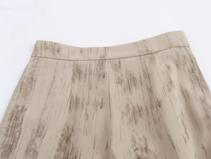Dettaglio dei pantaloni in lino beige con pieghe in vita e stampa a inchiostro marrone