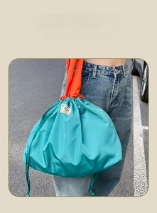 Detail showing dual side drawstring closure on a large turquoise and orange shopping bag