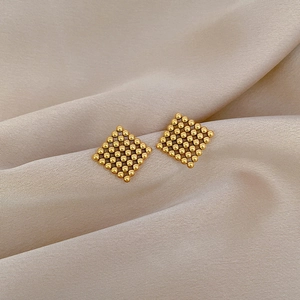 Minimalist square golden beaded stud earrings on elegant champagne silk fabric background