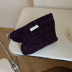 Close-up of purple tweed knit makeup bag with simple wish label on a white table
