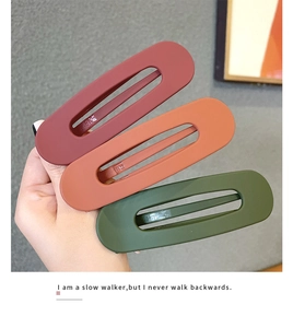 Three matte large hair clips in dark red, orange brown, and dark green held by hand